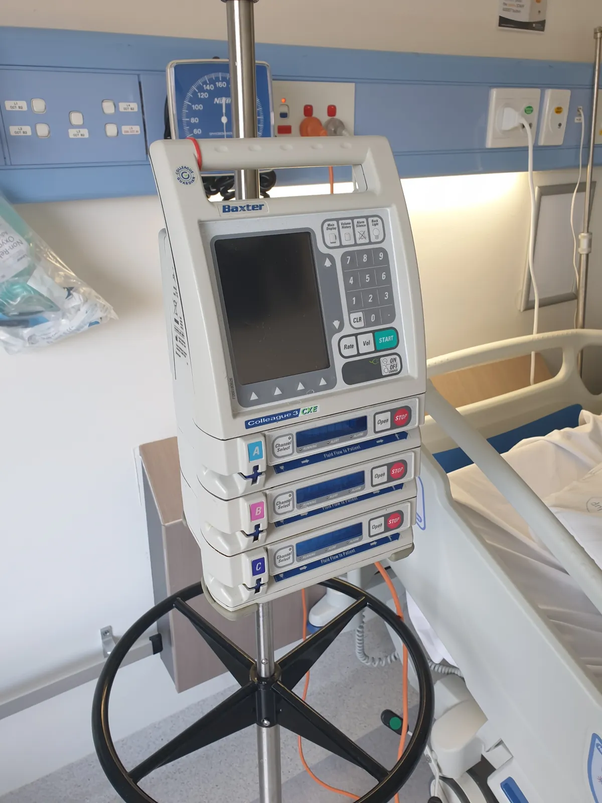 An infusion pump mounted on an IV pole beside a patient bed